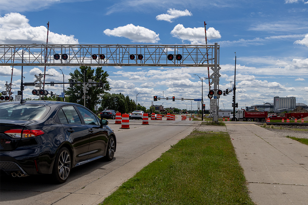 Car in foreground moving toward railroad intersection lined with traffic cones