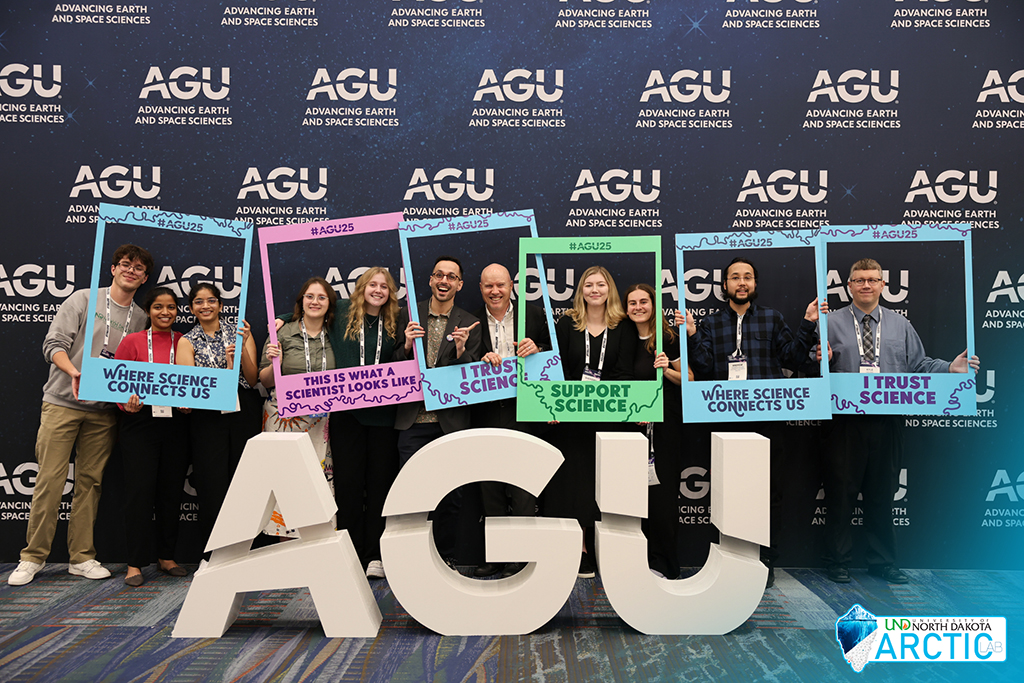 Timothy Pasch and students hold large novelty photo frames in front of Advancing Earth and Space Sciences conference backdrop