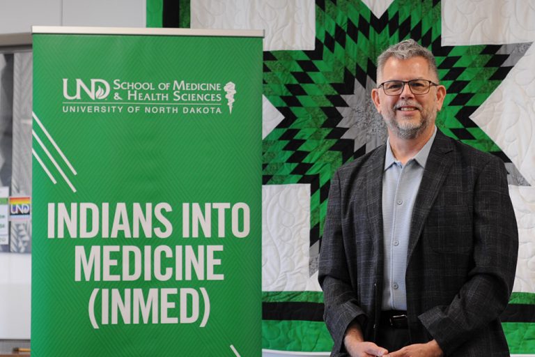 Melvin Monette-Barajas standing next to Indians into Medicine banner