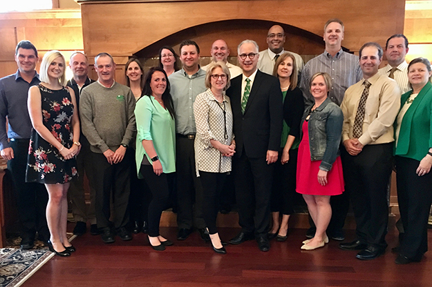 UND coach and Athletic Department staff members gathered on May 1 for a special dinner at the home of President Mark Kennedy and First Lady Debbie Kennedy (pictured center) to celebrate a previous academic year filled with conference championships and two national tournament appearances on the heels of a national championship in men’s hockey in 2015-16. Among the coaches present that night: Chris Logan, soccer; Kevin Galbraith, track& field; Dick Clay, cross country; Katie Martinson, women’s golf, Mark Pryor, volleyball, Travis Brewster, women’s basketball; Brian Jones, men’s basketball; Jordan Stevens, softball and Brad Berry, hockey. Head Football Coach Kyle “Bubba” Schweigert, who was interviewed for this story, was not present because he was on a recruiting trip. Photo courtesy of the Office of the UND President.