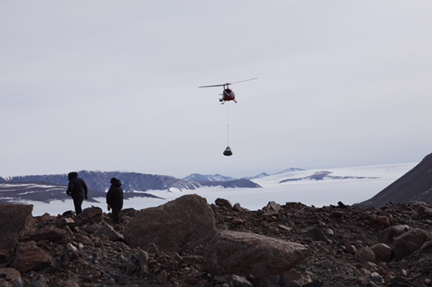 A helicopter carries part of a drilling rig from a campsite to a different site in the dry Antarctic valley.