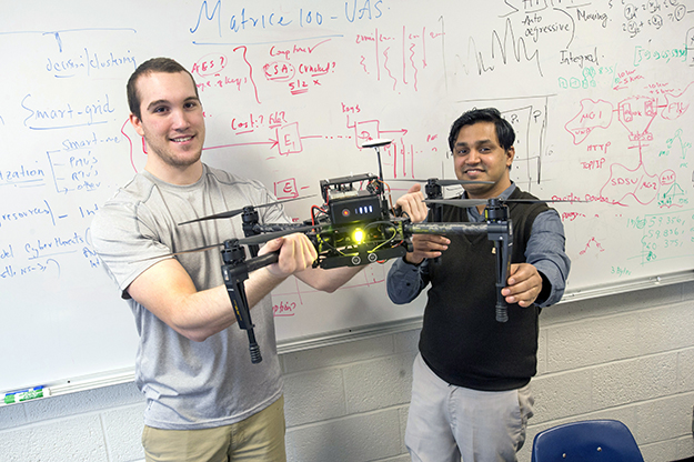 Elecrical engineering major Eric Horton (left) and his profess Prakash Ranganathan, work on a shophisticated unmanned aerial vehicale. Horton has been investigating cyberattacks on Global Positiong Systems datasets, a critial component in the navigation and control of these aircraft.