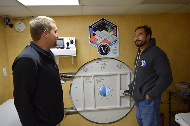 Travis Nelson, left, and Michael Castro stand next to the hatch leading to the outside world. Visible are the signatures of past mission crew members. Photo by Dima Williams/UND Today.