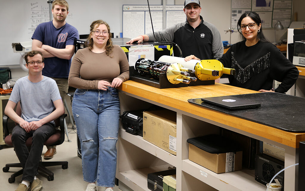 five people pose around scientific equipment