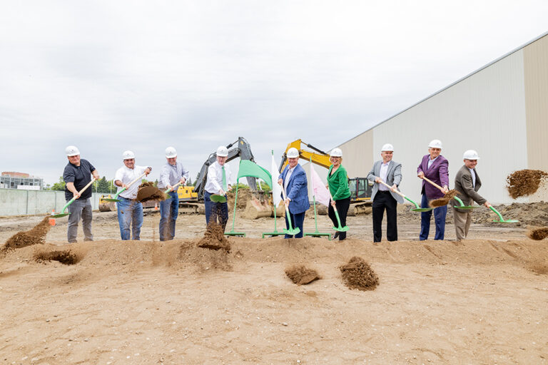 people throw shovels of dirt at a groundbreaking
