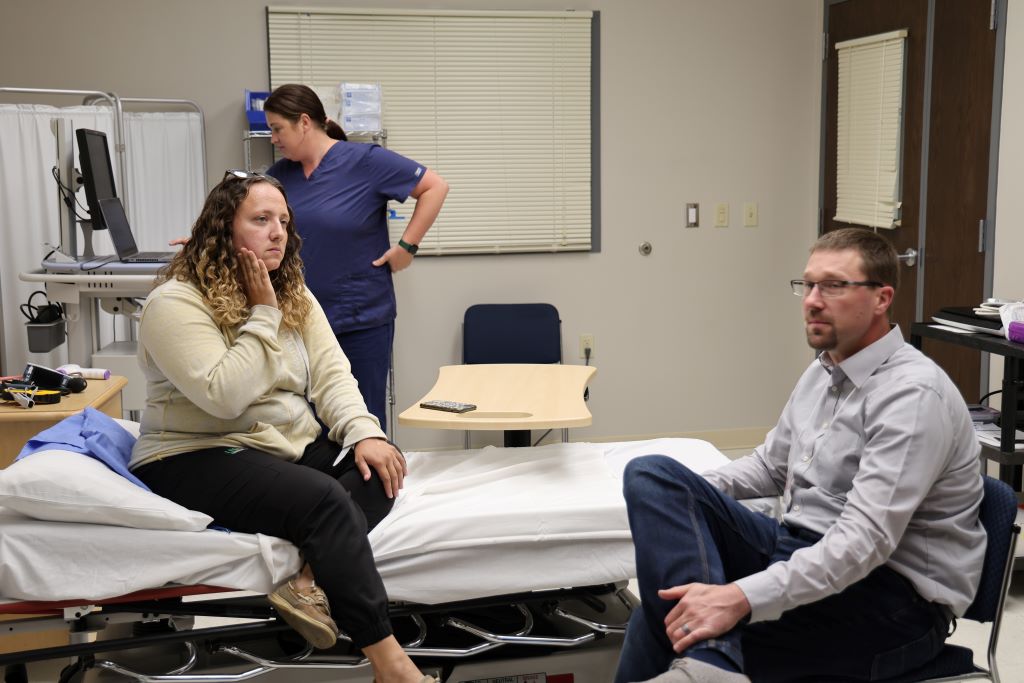 a patient in pain sits on doctor's table with doctor and nurse in view