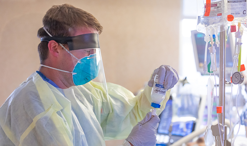 Person in full protective equipment drawing from vial