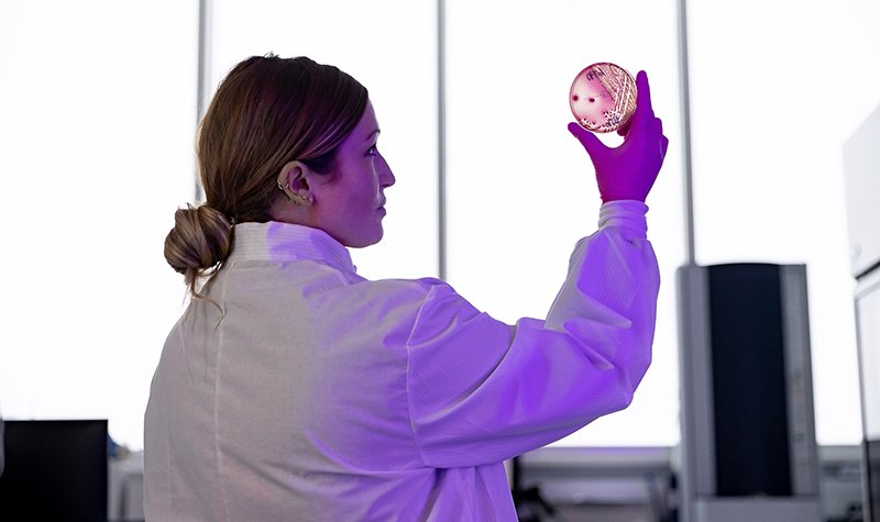Kelli Maddock in white coat holds petri dish