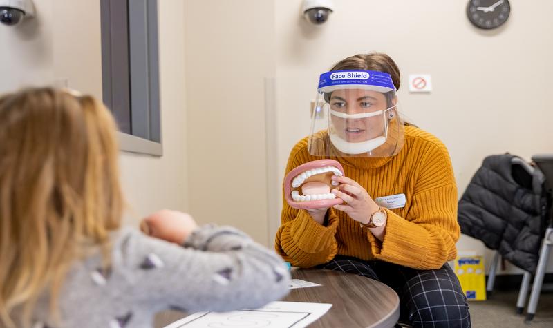 Teacher wearing clear face covering holding fake set of teeth