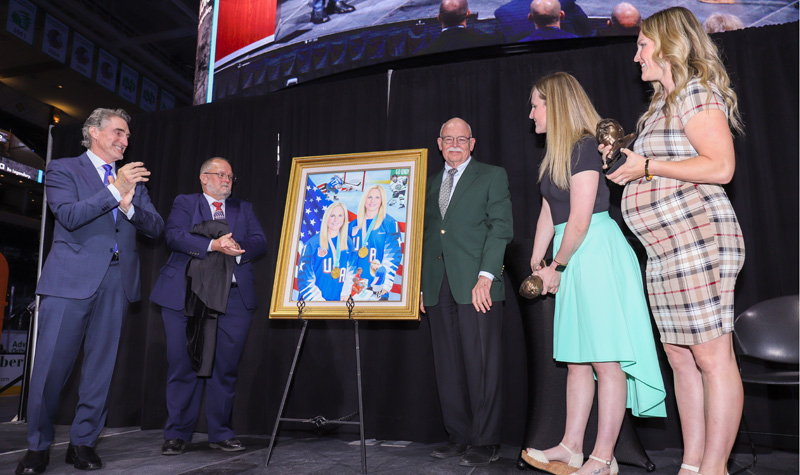 Gov. Doug Burgum, State Historical Society Director Bill Peterson, Secretary of State Al Jager, Monique Lamoureux-Morando and Jocelyne Lamoureux-Davidson at Ralph Engelstad Arena with painting of Lamoureux twins