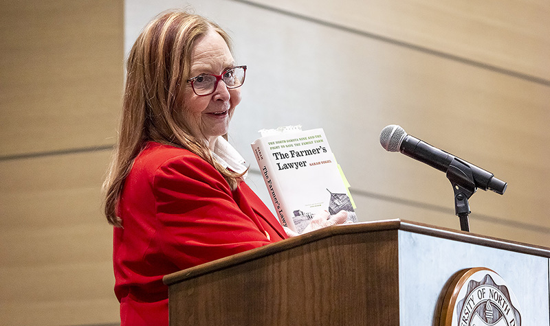 Sarah Vogel holds book while speaking from lectern