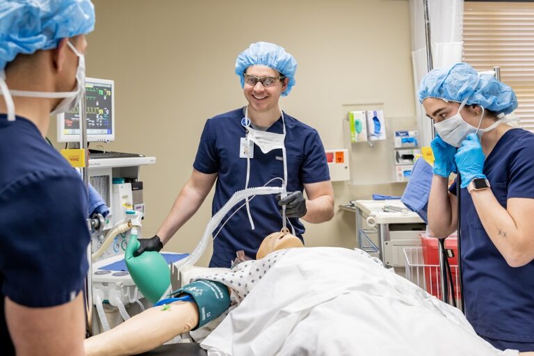 People in scrubs and protective equipment stand over simulated patient