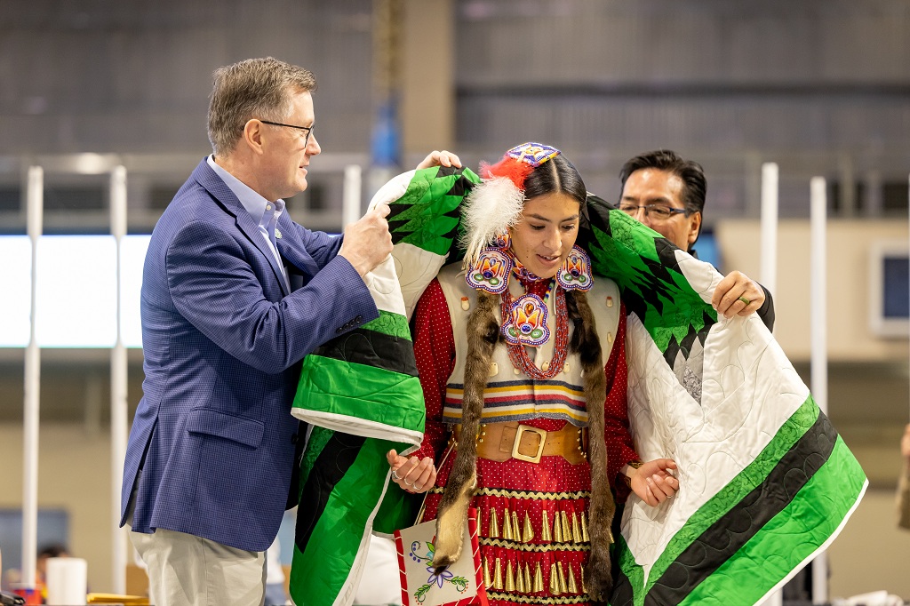 UND President Andy Armacost (left) helps drape a star quilt around the shoulders of UND student Eliana Malnourie.