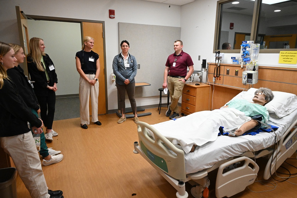 In a room with a SIM patient, participants in the Interprofessional Healthcare Conference discuss taking a team approach.