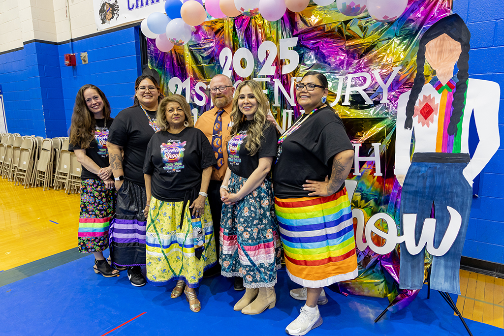 Julie Robinson, Lorena Brown-Joshua, Renuka de Silva, Byron Engberg, Mena de la Paz and Leora Fox-White stand in front of Native fashion show backdrop.