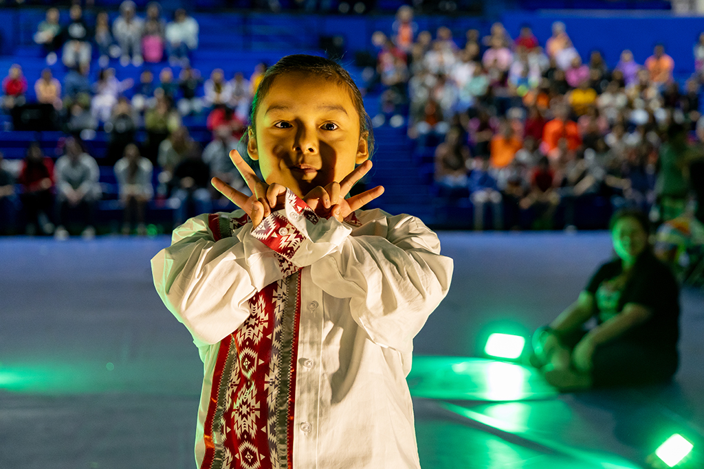 Boy wears colorful ribbon shirt as Native tradition in fashion show.