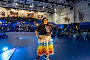 A young girl proudly shows her colorful ribbon skirt with tailing fringe.