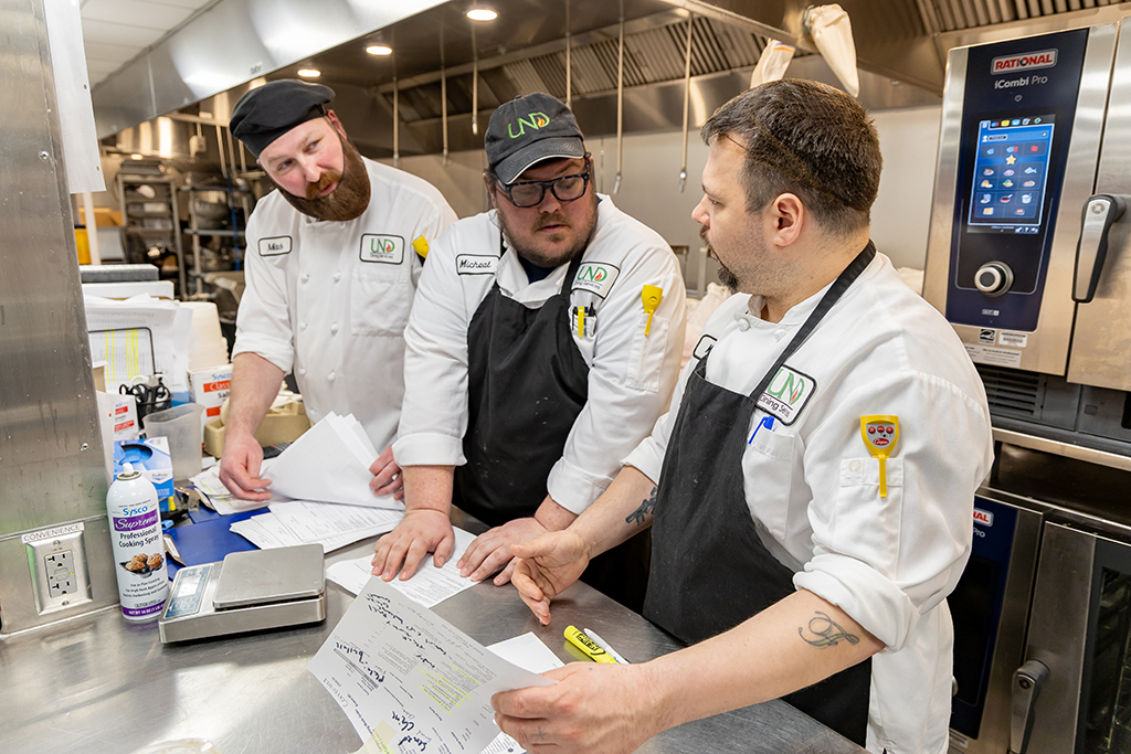 UND Catering chefs Mitch Vervalen, Micheal Longwell and Matt Fashingbauer stand at the counter and discuss the day's work.