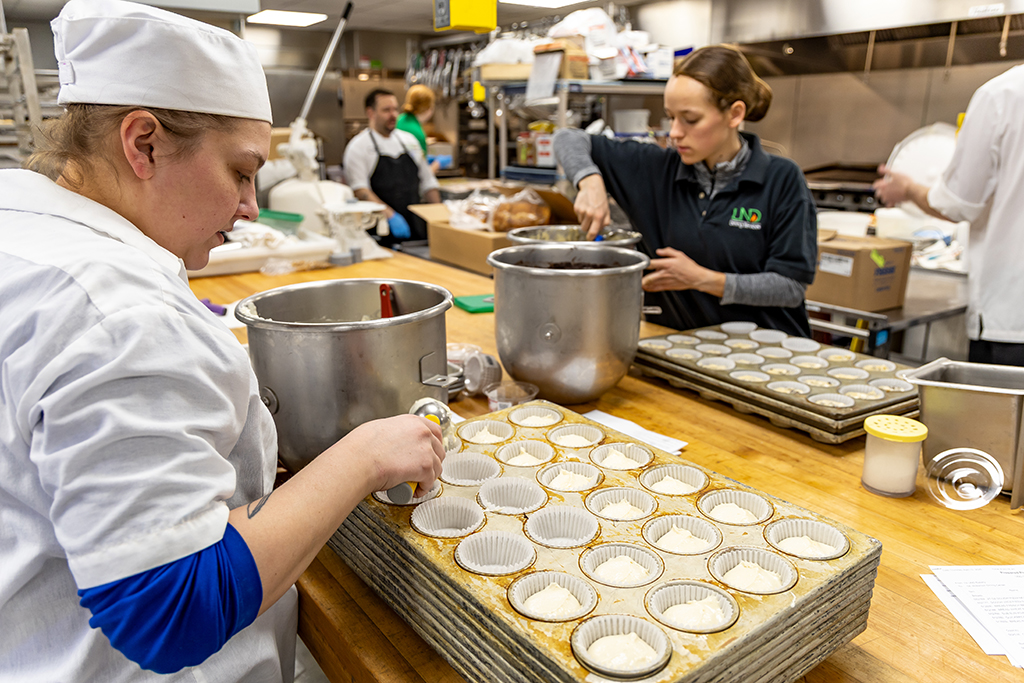 Bakery Manager Caylie Salge and a student scoop batter into the tins.