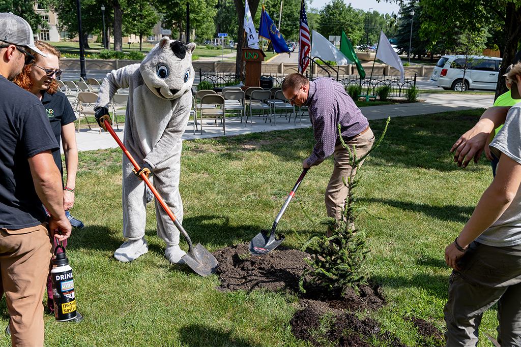 a man and a person in a squirrel mascot costume plant a tree