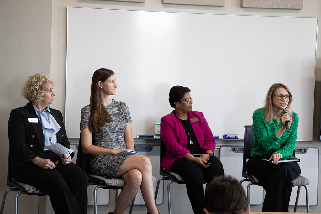 Randi Tanglen speaks with microphone as Lynette Krenelka, Beth Valentine and Madhavi Marasinghe look on