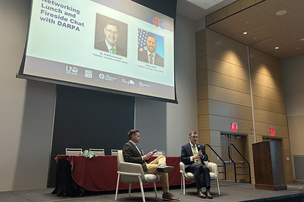 ARMACOST and President Phillip Smith speak on stage at the AI & Autonomy Conference at UND