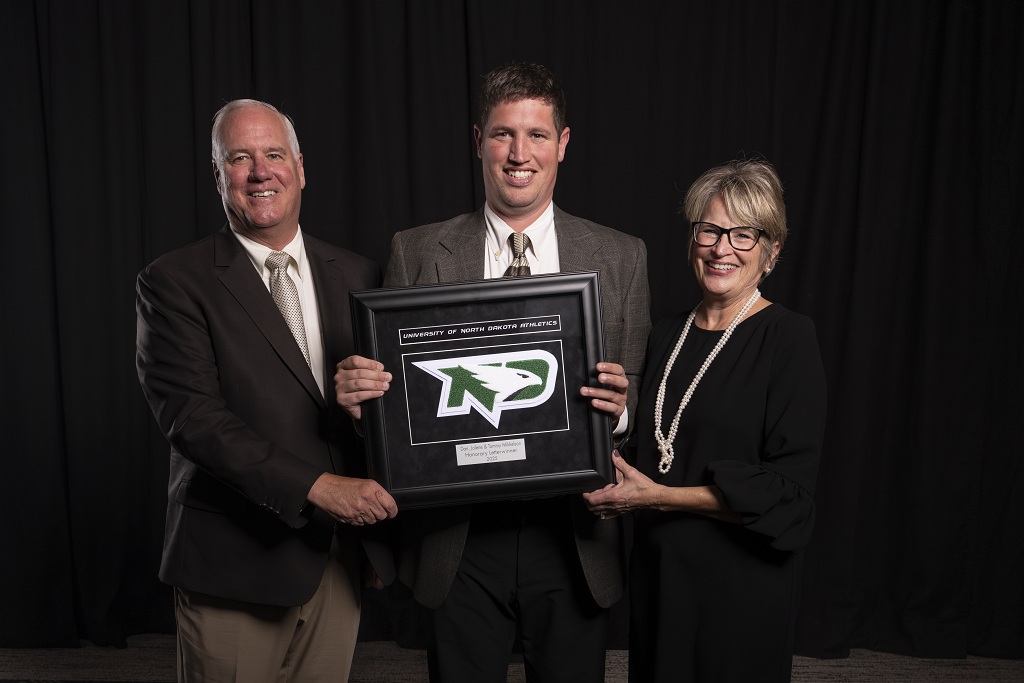 Dan, Tommy and Jolene Mikkelson hold the UND Letterwinners Association Honorary Award, which they were awarded in September.