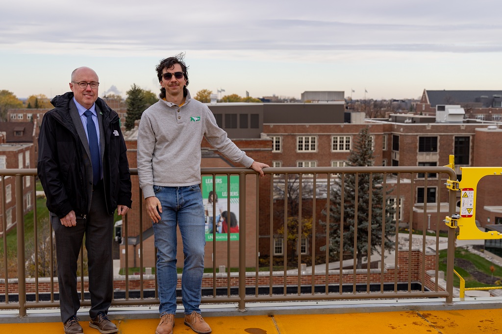 Two men stand on the roof of Witmer Hall, a building on the UND campus.