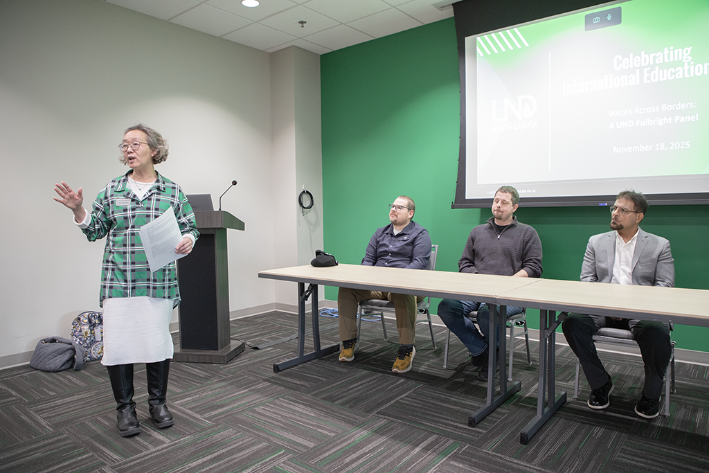 chu stands with panelists seated at table