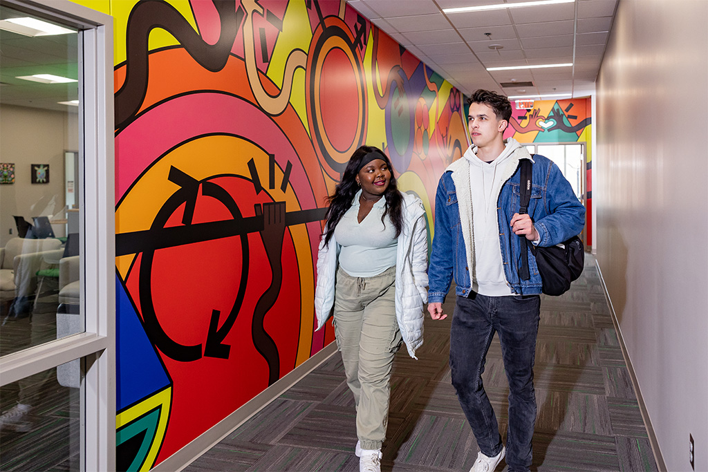 two students walking next to mural
