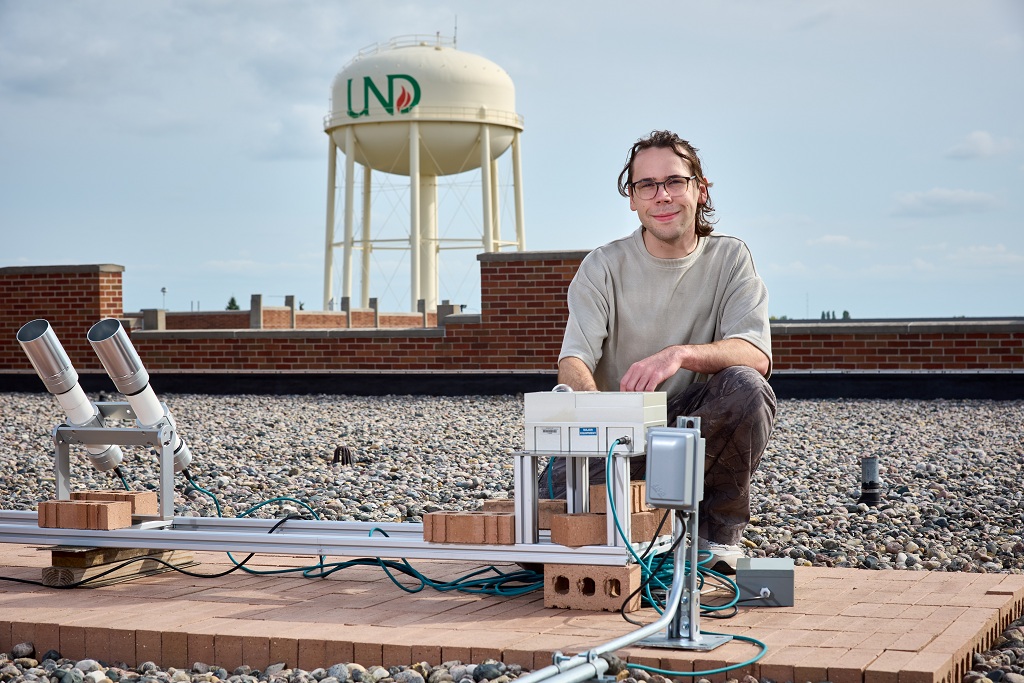 A man kneels on the roof of Witmer Hall behind some electronics equipment