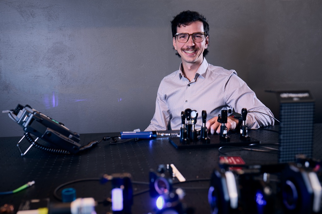 A man sits behind an optical table in a university lab