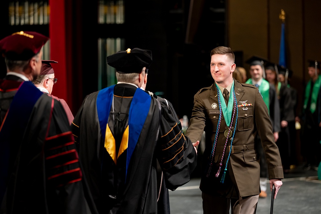 Army 2nd Lt. Casin Buckmeier shakes hands while crossing the stage during UND's Winter Commencement 2025.