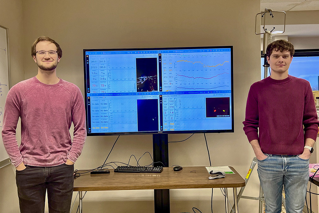 Conrad Slad (left) and Bryce Rickbeil (right) set up rooftop meteorological sensors on a tripod at Clifford Hall and process the resulting data streams, using live displays to visualize observations and quality-check measurements