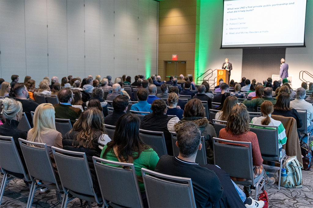 a crowd in a room listens to two presenters