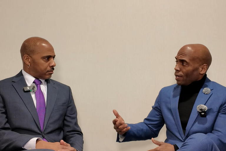 Tamba-Kuii Bailey and Yohuru Williams, both seated, converse against a plain backdrop.