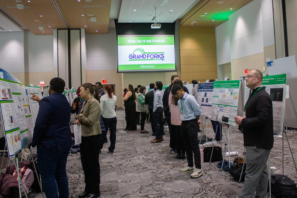 Students and attendees standing next to research posters in ballroom