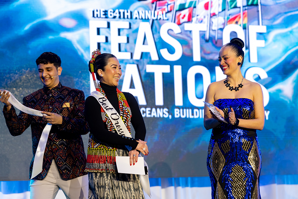 Woman on stage wearing a sash that says "best dressed" as two others look on