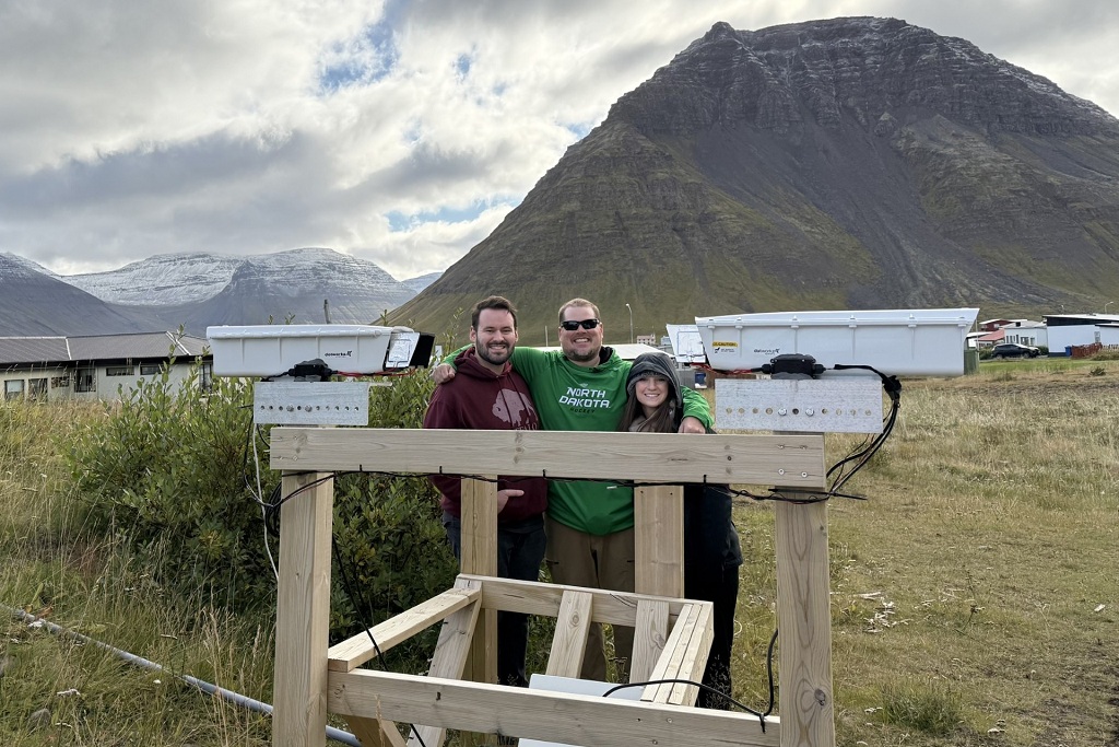 Three people stand by scientific instruments in the Icelandic countryside.