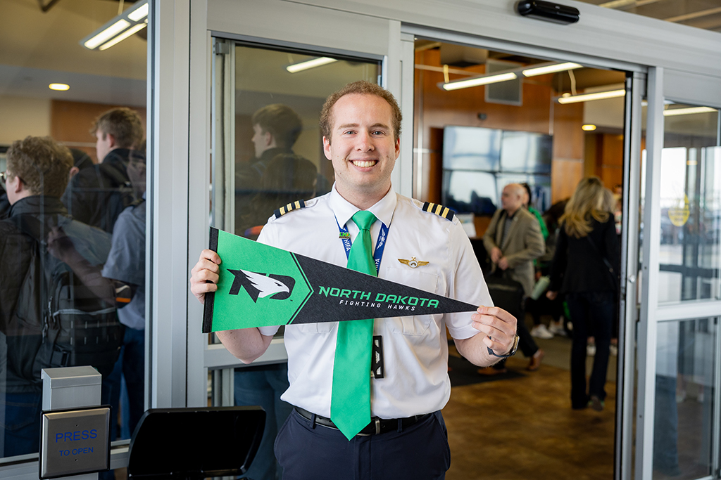 Pilot smiling, holding up North Dakota Fighting Hawks pennant