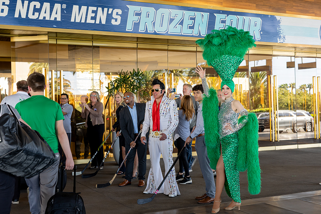 People, including showgirl dressed in green and an Elvis impersonator, welcome the team to the arena