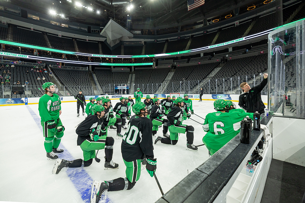 Fighting Hawks team kneel during practice, watch coach draw a play