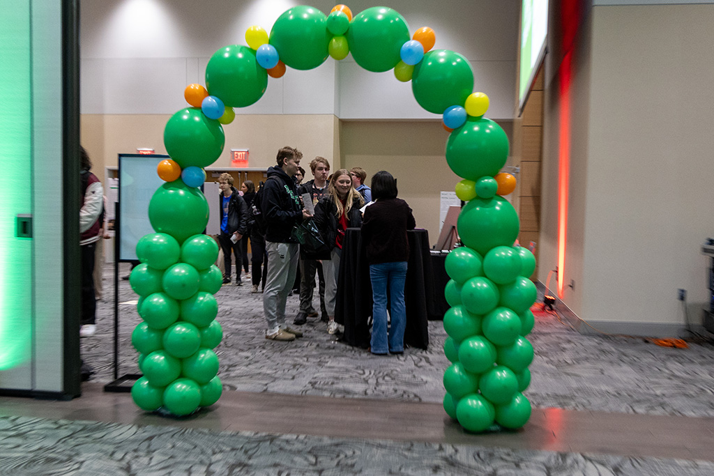 Students gather around a check-in table beneath a large green balloon arch