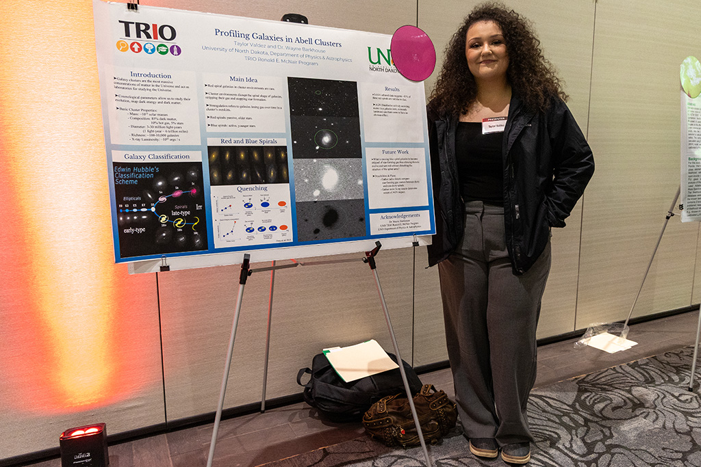 student stands beside a research poster