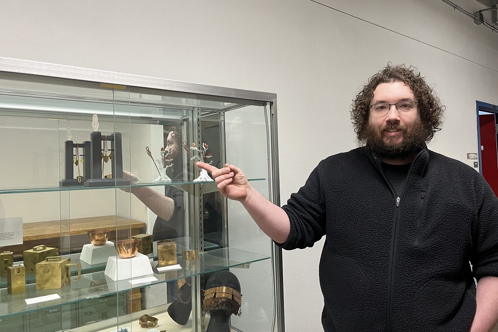 Ryan Johnson stands by glass enclosure showcasing his artwork