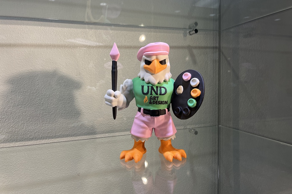 3D-printed artwork depicting a hawk holding artists' tools and wearing a "UND Art & Design" T-shirt.