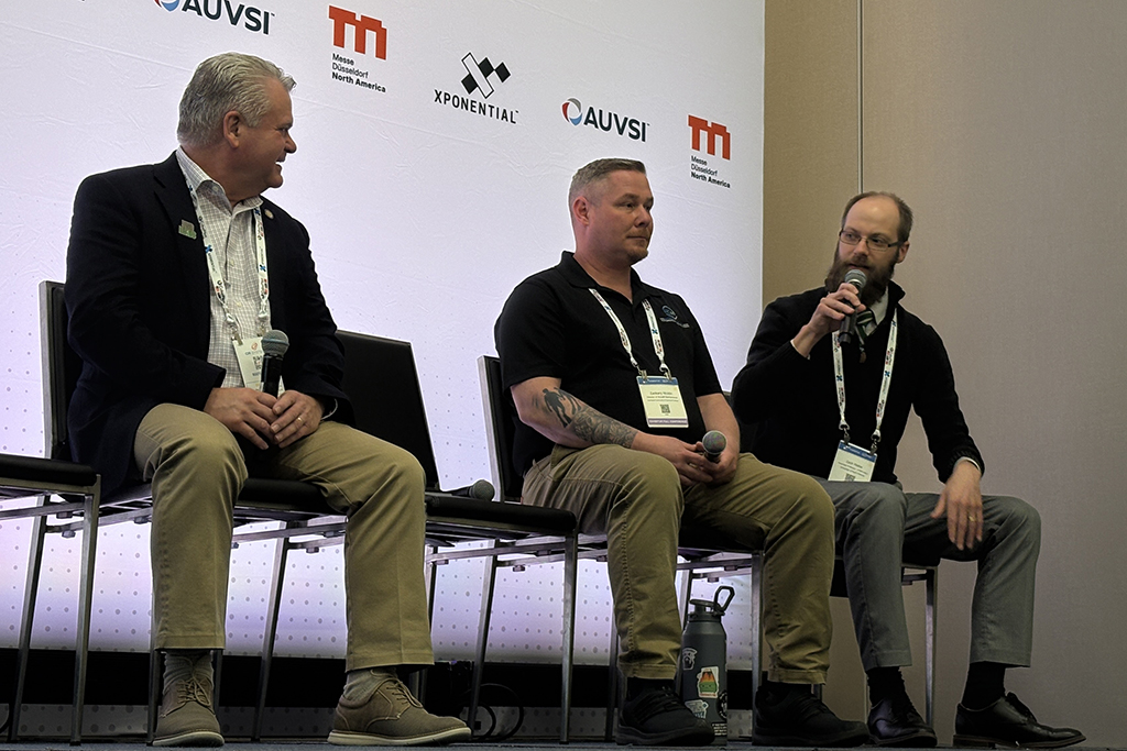 Jeff Barta, Zack Nicklin and Zach Waller sitting as members of panel at Xponential conference, with Waller speaking into microphone.