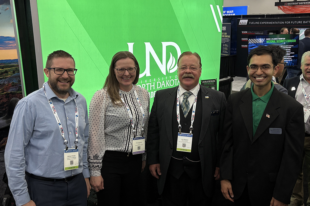 Mike Haman, Amy Whitney, Joe Wiegand as Teddy Roosevelt and Vigneshwar Parameshwar pose for photo in front of UND backdrop