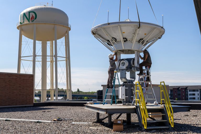 a crane lowering antenna reflector, two men attach it to base