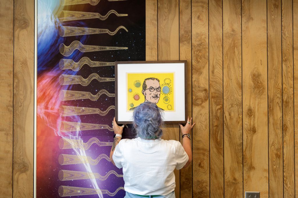 Sarah Heitkamp adjusts framed artwork on wood paneled wall